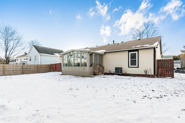 snow covered back of property with cooling unit and a sunroom