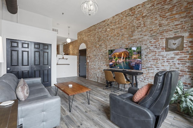 living room with a high ceiling, an inviting chandelier, brick wall, and hardwood / wood-style flooring