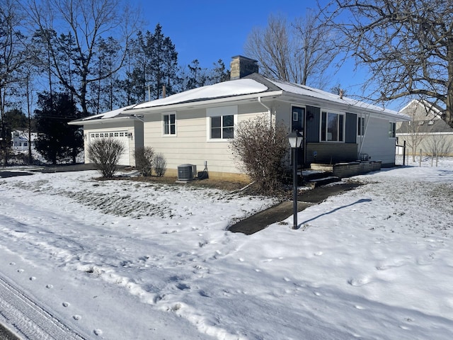 snow covered back of property featuring central AC unit and a garage