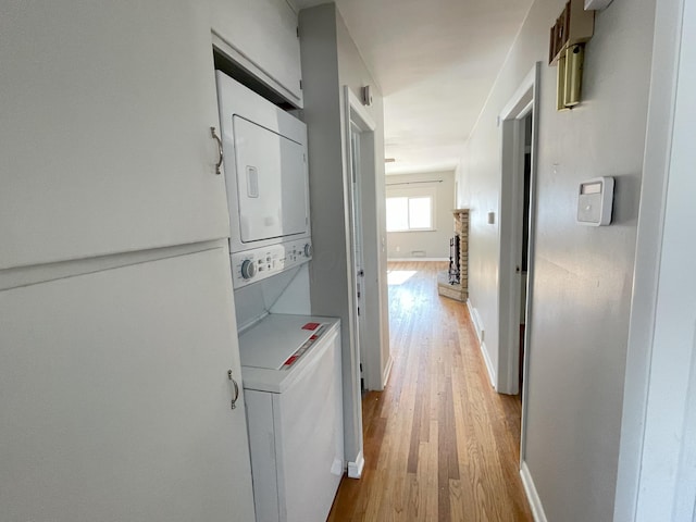 hallway with stacked washer and clothes dryer and light hardwood / wood-style flooring