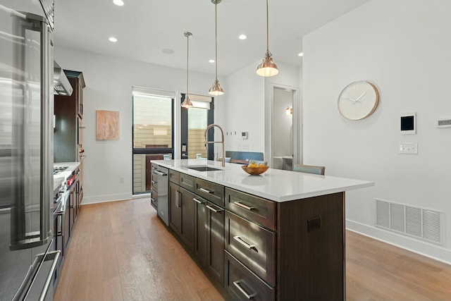 kitchen featuring pendant lighting, sink, dark brown cabinets, light hardwood / wood-style floors, and a center island with sink