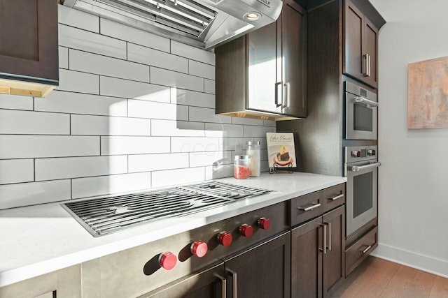 kitchen featuring oven, decorative backsplash, light hardwood / wood-style floors, gas stovetop, and wall chimney exhaust hood