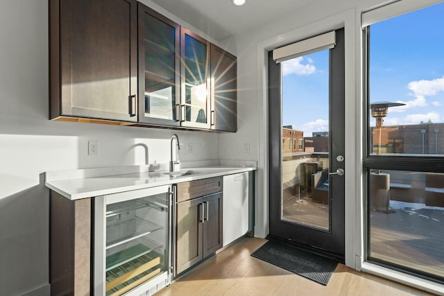 bar featuring sink, wine cooler, stainless steel dishwasher, dark brown cabinetry, and light hardwood / wood-style floors