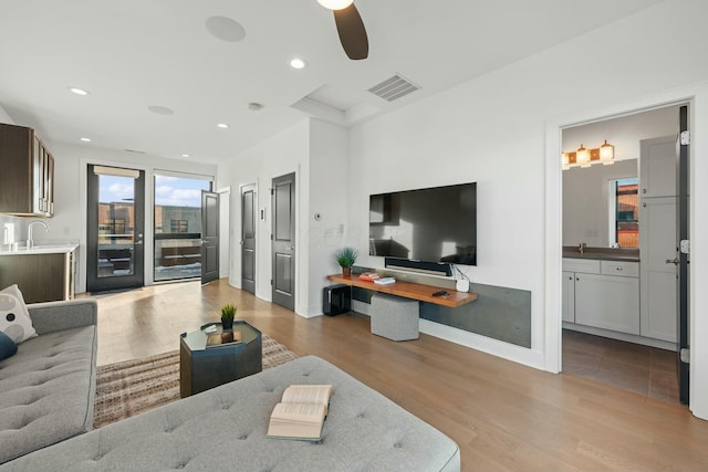 living room with ceiling fan, sink, and light wood-type flooring