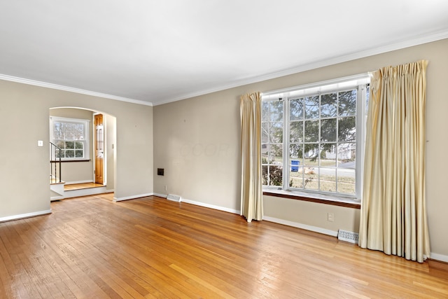 unfurnished living room with ornamental molding, arched walkways, light wood-style flooring, and baseboards