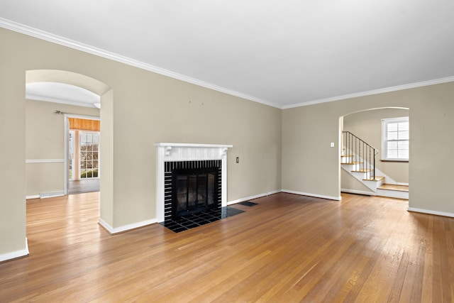 unfurnished living room featuring a wealth of natural light, arched walkways, a fireplace, and hardwood / wood-style flooring