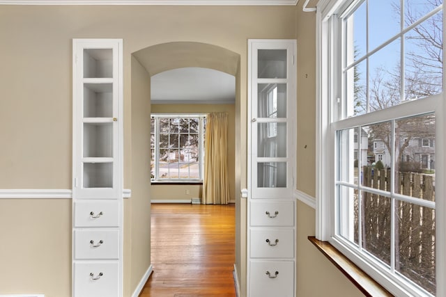 corridor with baseboards, arched walkways, and wood finished floors