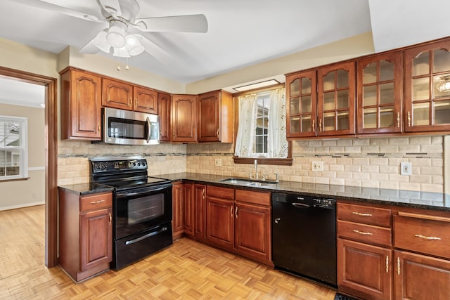 kitchen featuring a sink, dark stone counters, black appliances, tasteful backsplash, and glass insert cabinets