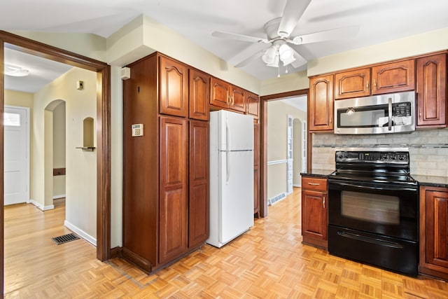 kitchen with arched walkways, visible vents, stainless steel microwave, black range with electric stovetop, and freestanding refrigerator