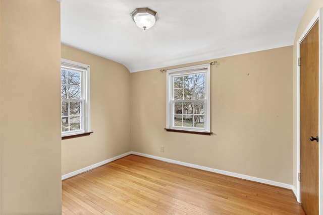 empty room featuring lofted ceiling, light wood-style flooring, and baseboards