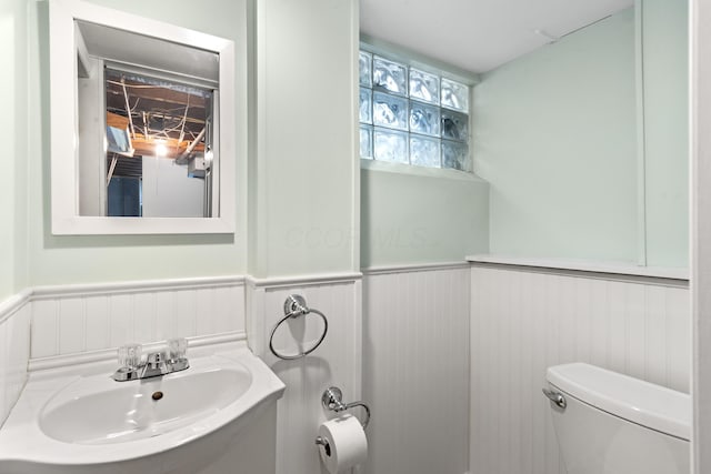 bathroom featuring toilet, a wainscoted wall, and a sink