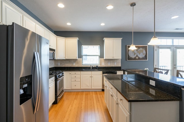 kitchen with decorative light fixtures, stainless steel appliances, dark stone countertops, light hardwood / wood-style floors, and sink