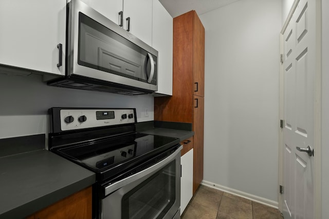 kitchen featuring stainless steel appliances, dark tile patterned flooring, and white cabinets