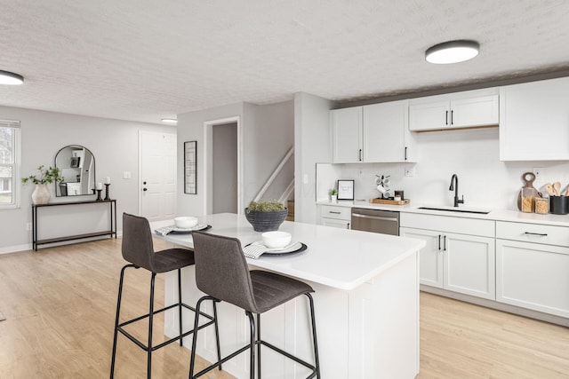 kitchen with sink, light hardwood / wood-style flooring, white cabinetry, a textured ceiling, and stainless steel dishwasher