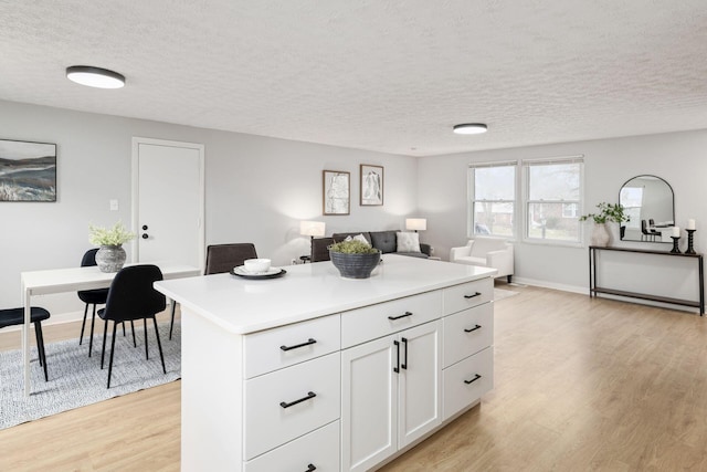 kitchen with white cabinetry, a center island, a textured ceiling, and light wood-type flooring