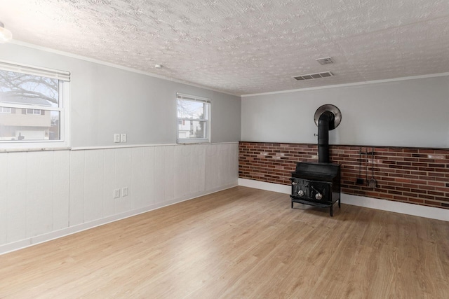 unfurnished living room with light wood-type flooring, ornamental molding, a textured ceiling, and a wood stove