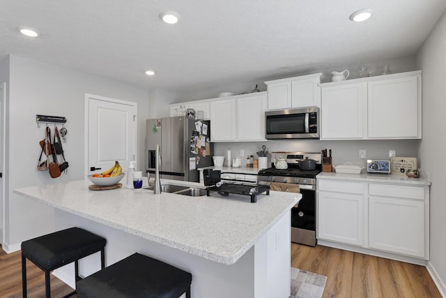 kitchen with a breakfast bar, white cabinetry, appliances with stainless steel finishes, and light hardwood / wood-style flooring