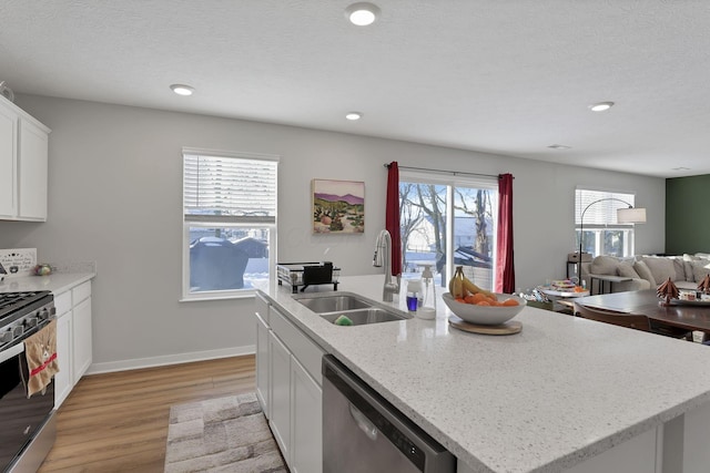 kitchen with appliances with stainless steel finishes, a kitchen island with sink, white cabinets, light hardwood / wood-style flooring, and sink