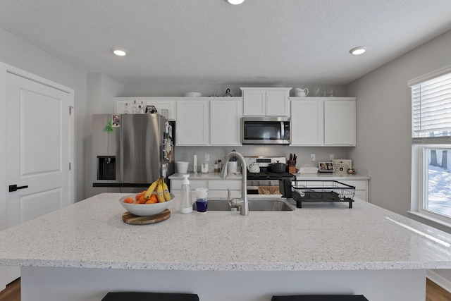 kitchen with white cabinetry, stainless steel appliances, a kitchen island with sink, a textured ceiling, and sink