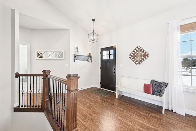 entrance foyer with an inviting chandelier, vaulted ceiling, and dark hardwood / wood-style floors