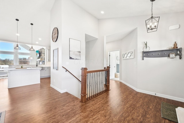 corridor with dark wood-type flooring, high vaulted ceiling, and a chandelier