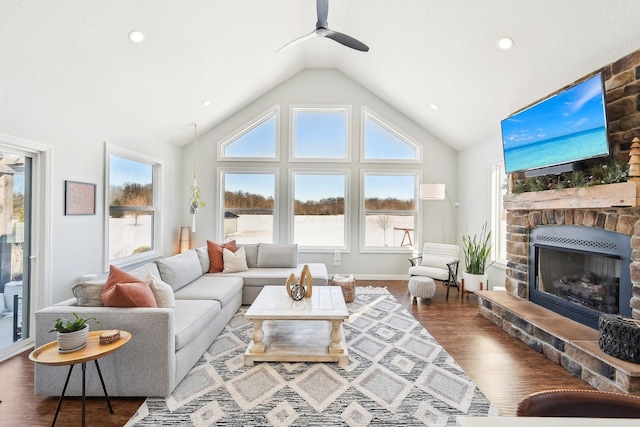 living room featuring a stone fireplace, vaulted ceiling, dark hardwood / wood-style floors, and ceiling fan