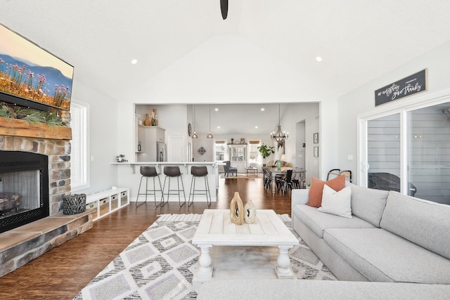 living room featuring dark wood-type flooring, a fireplace, vaulted ceiling, and a notable chandelier