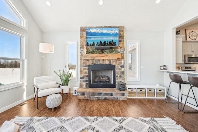 living area with dark wood-type flooring, vaulted ceiling, and a stone fireplace