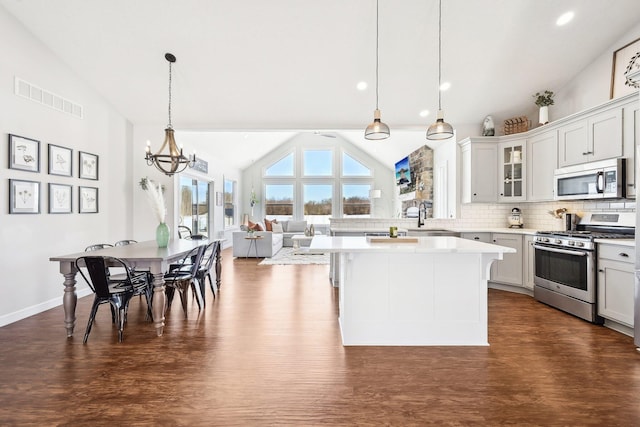 kitchen featuring lofted ceiling, appliances with stainless steel finishes, backsplash, a kitchen island, and decorative light fixtures