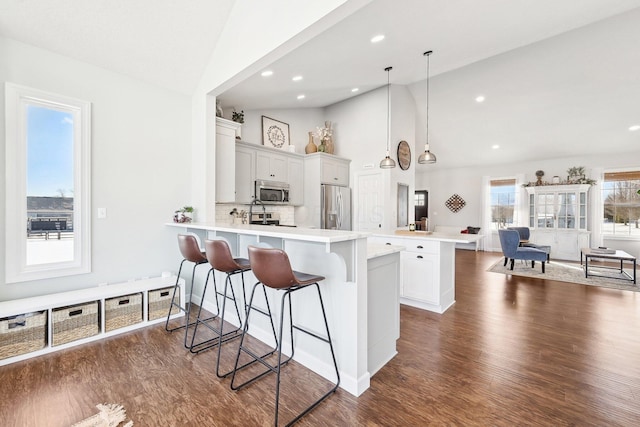 kitchen with a breakfast bar area, hanging light fixtures, stainless steel appliances, white cabinets, and decorative backsplash