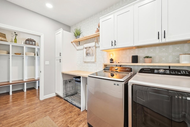 clothes washing area with cabinets, light hardwood / wood-style flooring, and washing machine and clothes dryer