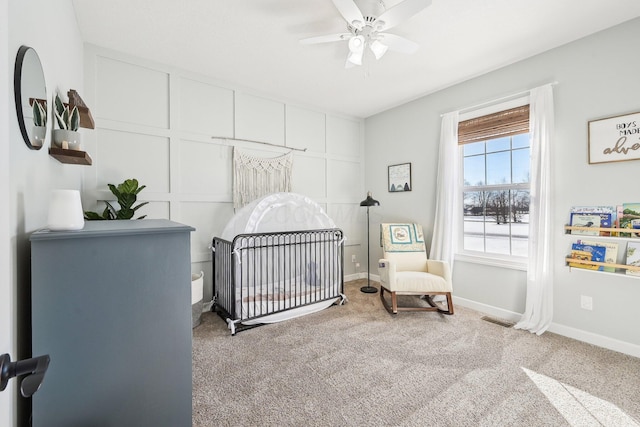 bedroom featuring a nursery area, carpet, and ceiling fan