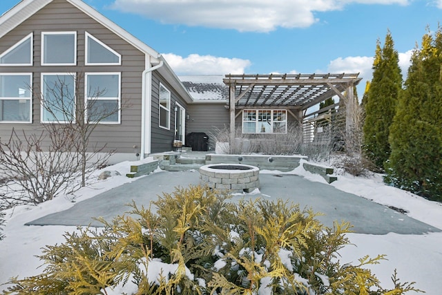 snow covered back of property with a pergola and a fire pit