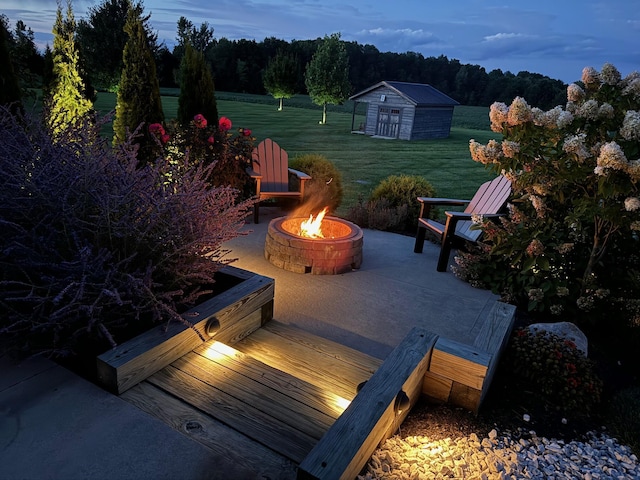 patio terrace at dusk featuring a storage shed, a wooden deck, a yard, and a fire pit