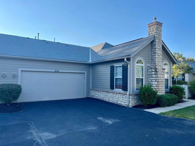 view of side of home featuring a garage, a chimney, aphalt driveway, and roof with shingles