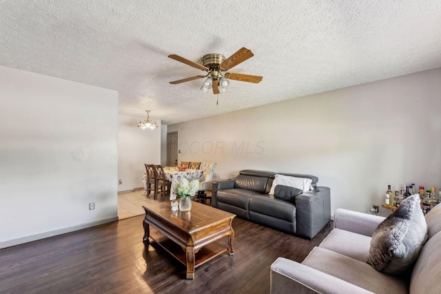 living room with dark wood-type flooring, ceiling fan with notable chandelier, and a textured ceiling