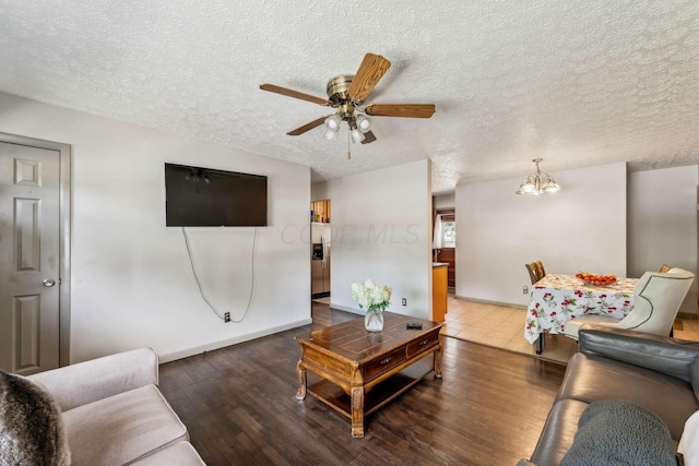 living room with ceiling fan with notable chandelier, dark wood-type flooring, and a textured ceiling