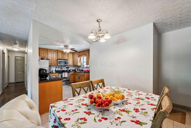 tiled dining space featuring ceiling fan with notable chandelier and a textured ceiling