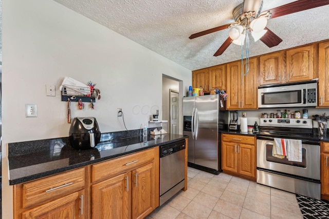 kitchen featuring ceiling fan, dark stone countertops, light tile patterned flooring, appliances with stainless steel finishes, and a textured ceiling