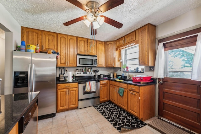 kitchen featuring stainless steel appliances, light tile patterned flooring, dark stone countertops, a textured ceiling, and sink