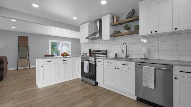 kitchen with white cabinets, wall chimney exhaust hood, stainless steel appliances, sink, and kitchen peninsula