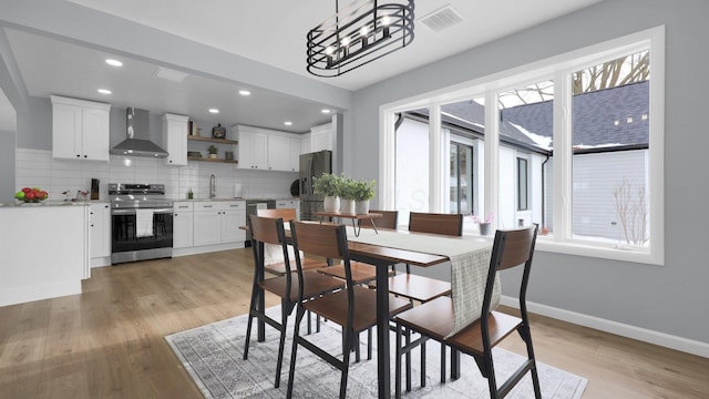 dining area with light wood-type flooring, an inviting chandelier, and sink