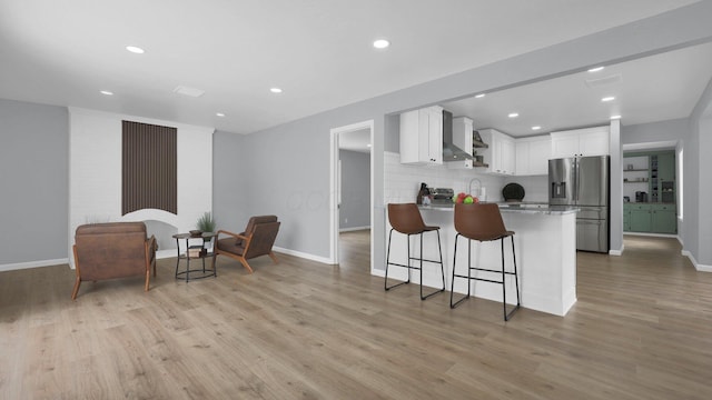 kitchen with tasteful backsplash, wall chimney range hood, light hardwood / wood-style floors, stainless steel refrigerator with ice dispenser, and white cabinetry