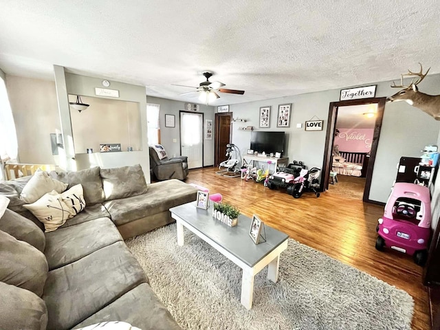 living room with ceiling fan, wood-type flooring, and a textured ceiling