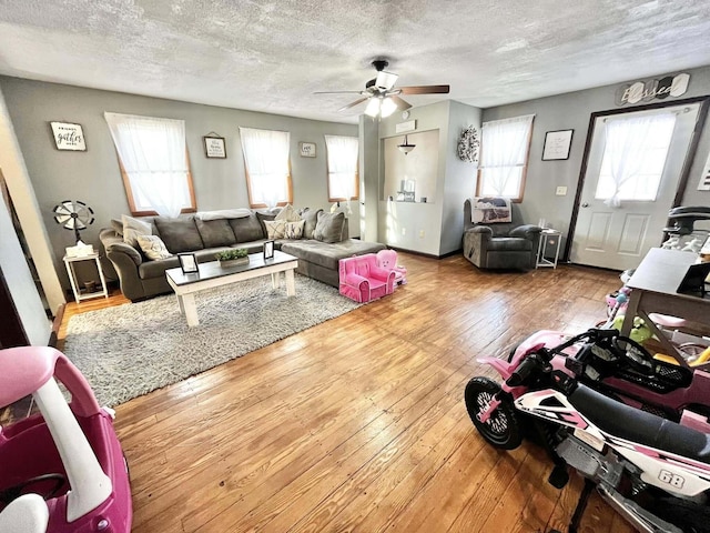 living room with a textured ceiling, ceiling fan, and wood-type flooring