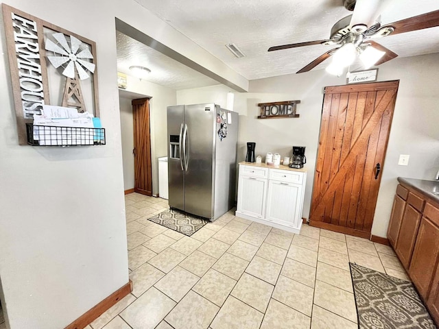 kitchen with stainless steel refrigerator with ice dispenser, ceiling fan, light tile patterned flooring, and a textured ceiling