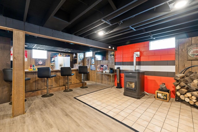 basement with bar, a healthy amount of sunlight, a wood stove, and white fridge with ice dispenser