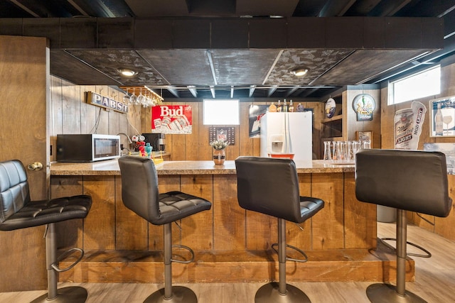 bar featuring white refrigerator with ice dispenser, light wood-type flooring, and wood walls