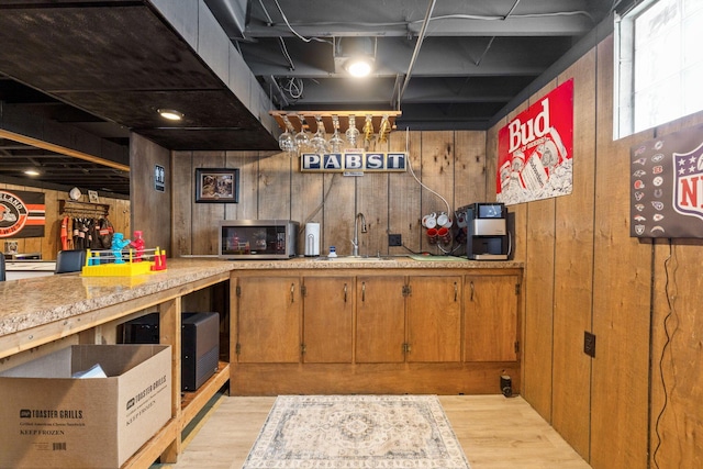 kitchen with wooden walls, sink, and light wood-type flooring