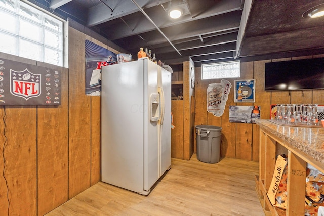 kitchen with wooden walls, light stone countertops, white fridge with ice dispenser, and light wood-type flooring